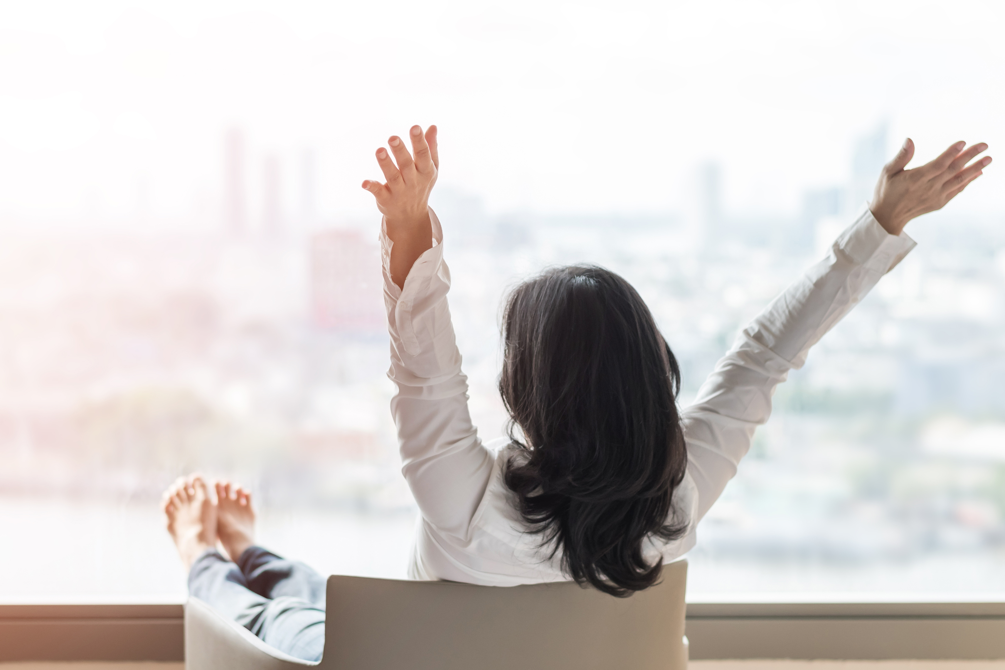 A woman raises her arms in the air overlooking a city skyline